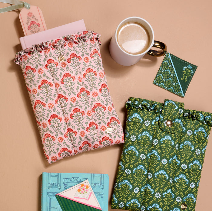 Two patterned pouches, a white coffee mug, a green cardholder, and two floral notebooks rest on beige—perfect for gifting with The Darling Effect’s Petals & Pages Corner Keeper Fabric Bookmark. A charming treat for any book lover!.