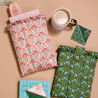 Two patterned pouches, a white coffee mug, a green cardholder, and two floral notebooks rest on beige—perfect for gifting with The Darling Effect’s Petals & Pages Corner Keeper Fabric Bookmark. A charming treat for any book lover!.