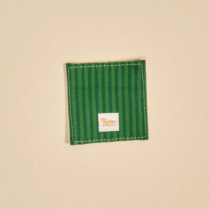 The Darling Effect’s Petals & Pages Corner Keeper Fabric Bookmark features vertical green stripes, white stitching, and a small white label—an ideal gift for book lovers—elegantly displayed on a plain beige background.