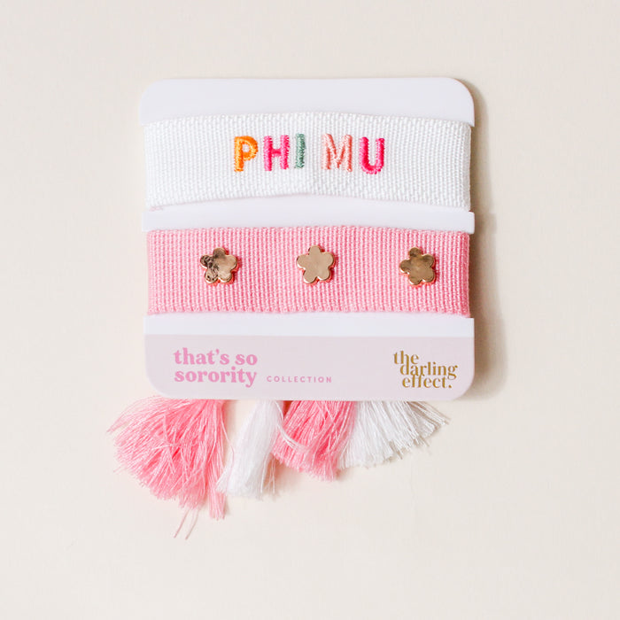 The Darling Effect's Phi Mu Woven Bracelet Set is the perfect sorority gift, featuring a white bracelet with colorful woven PH MU, a pink bracelet with gold flower charms, and pink and white tassel bracelets on a white card.