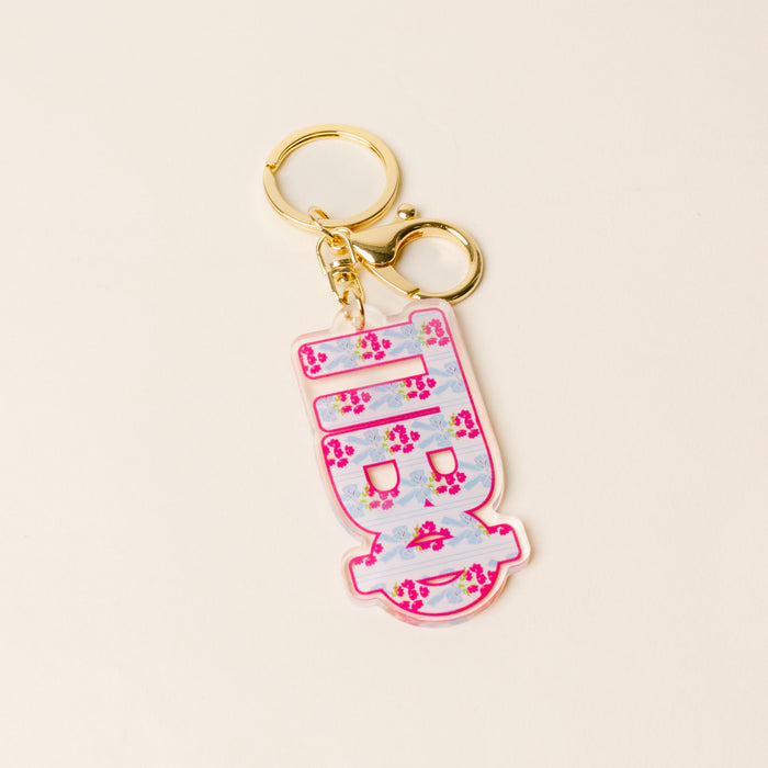 The Darling Effect’s Pi Beta Phi Oh So Fancy Letter Acrylic Keychain features a gold ring and a pastel pink and blue floral charm with a stylized Greek letter, displayed on a light beige background.