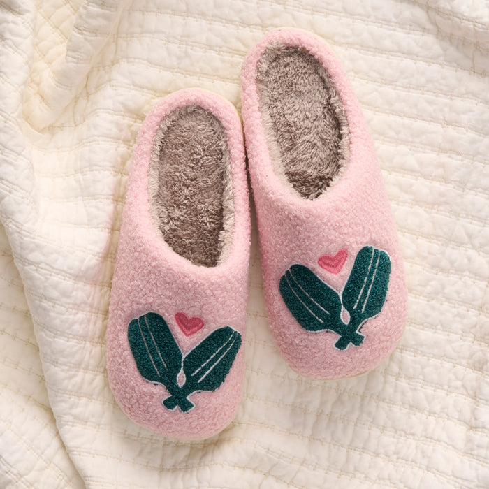 The-darling-effect Pickleball Paddles Fuzzy Slippers: cozy pink slip-ons with soft gray lining, green leaf accents, and a small pink heart on each, shown on a textured cream-colored quilt.