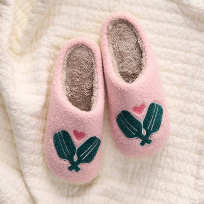 The-darling-effect Pickleball Paddles Fuzzy Slippers: cozy pink slip-ons with soft gray lining, green leaf accents, and a small pink heart on each, shown on a textured cream-colored quilt.