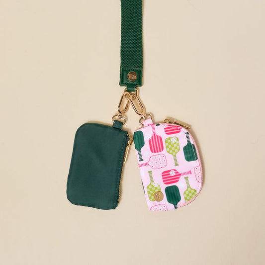 The-darling-effect Pickleball Party Dynamic Duo Pouch Wristlet features two small zippered pouches—one in forest green, the other with a pink pickleball paddle print—hanging from a green strap for a playful way to carry your essentials.
