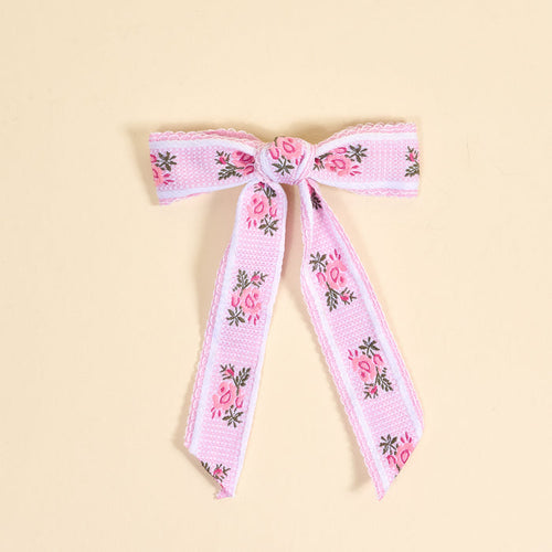 The Darling Effect's Pink Heirloom Rosette Hair Bow features pink and white ribbon with embroidered flowers and green leaves, adding charm to your hair accessories collection. Shown on a neutral beige background.