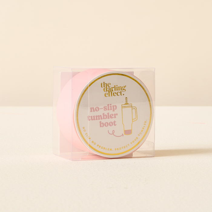 The Darling Effect Pink Tumbler Silicone Boot features gold trim and "the darling effect" text. This no-slip tumbler protector comes displayed in a clear plastic box.