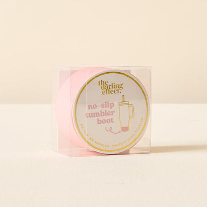 The Darling Effect Pink Tumbler Silicone Boot features gold trim and "the darling effect" text. This no-slip tumbler protector comes displayed in a clear plastic box.