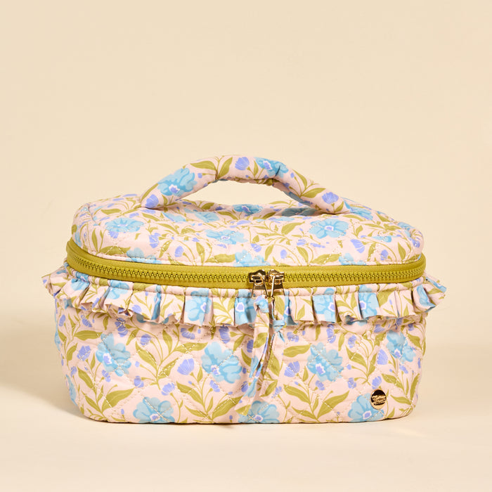The Darling Effect’s Poppin' Petals Aqua Glam & Go Quilted Cosmetic Bag features a floral design, green leaves, light blue blooms, ruffled trim, a yellow zipper, and top handle—all on a beige background.