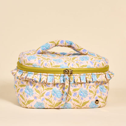 The Darling Effect’s Poppin' Petals Aqua Glam & Go Quilted Cosmetic Bag features a floral design, green leaves, light blue blooms, ruffled trim, a yellow zipper, and top handle—all on a beige background.
