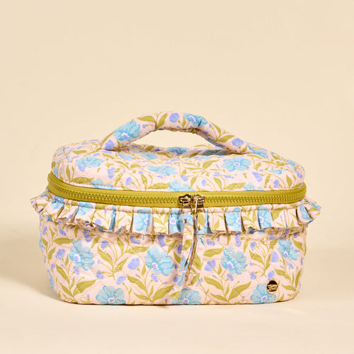 The Darling Effect’s Poppin' Petals Aqua Glam & Go Quilted Cosmetic Bag features a floral design, green leaves, light blue blooms, ruffled trim, a yellow zipper, and top handle—all on a beige background.