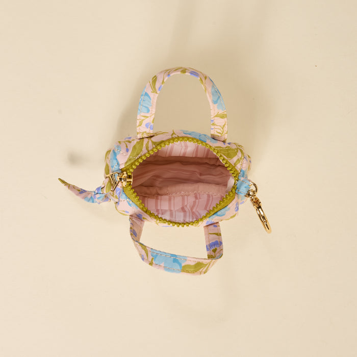 The Darling Effect’s Poppin' Petals Aqua Itty Bitty Duffle Bag Charm is a small fabric handbag with pastel florals, gold clasp, and two handles. An open zipper reveals its pink lining for a pop of color and style.