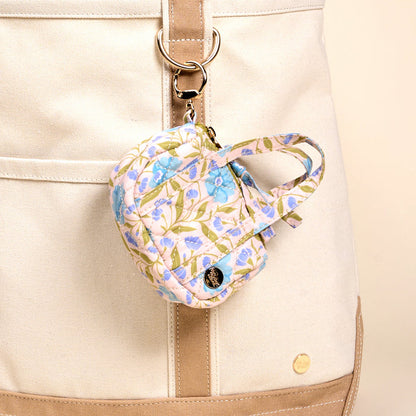 The Darling Effect's Poppin' Petals Aqua Itty Bitty Duffle Bag Charm features a quilted floral pouch with blue flowers and green leaves, attached by a metal clip for a stylish and charming tote bag accessory.