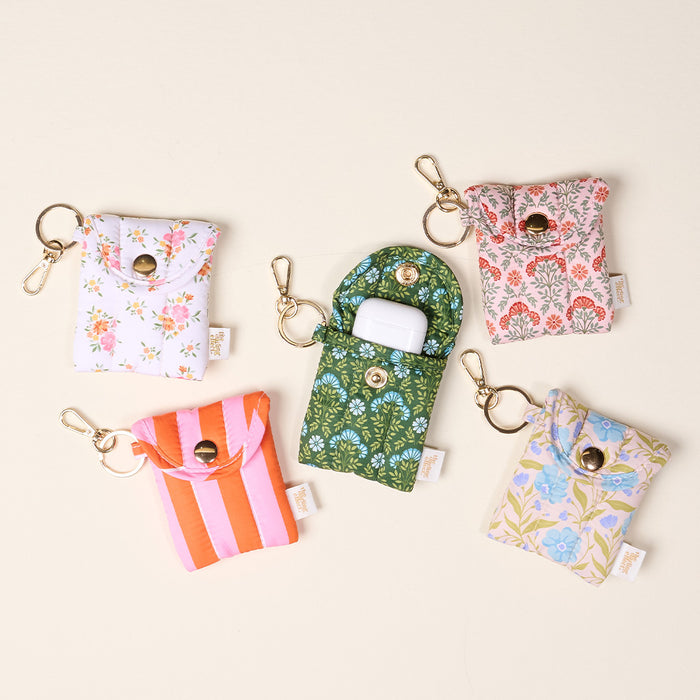 Five Poppin' Petals Aqua Puffy Earbud Cases by The Darling Effect have metal clasps and colorful floral or striped designs. The open green case at the center displays a pair of white wireless earbuds inside.