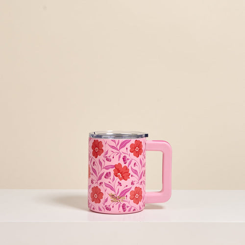The Darling Effect's Poppin' Petals Hot Pink 14 oz Insulated Mug, featuring red and pink floral and leafy designs with a large handle, sits on a white surface. Its double-wall insulation keeps drinks hot or cold longer.