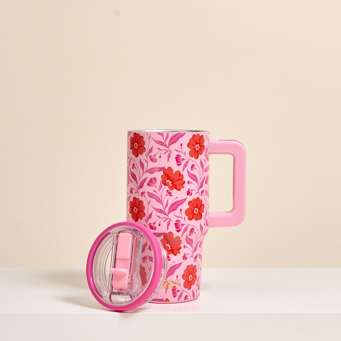 The Darling Effect’s Poppin' Petals Hot Pink 20 oz Lifestyle Flip Straw Tumbler, with red and pink floral designs and a matching pink lid with clear center, stands upright on a white surface against a beige background.