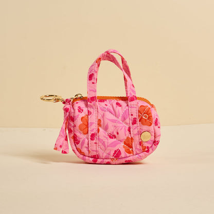 The Darling Effect’s Poppin' Petals Hot Pink Itty Bitty Duffle Bag Charm is a small quilted floral coin purse with two handles, zipper closure, and gold keychain clip—stylishly shown on a plain beige background.