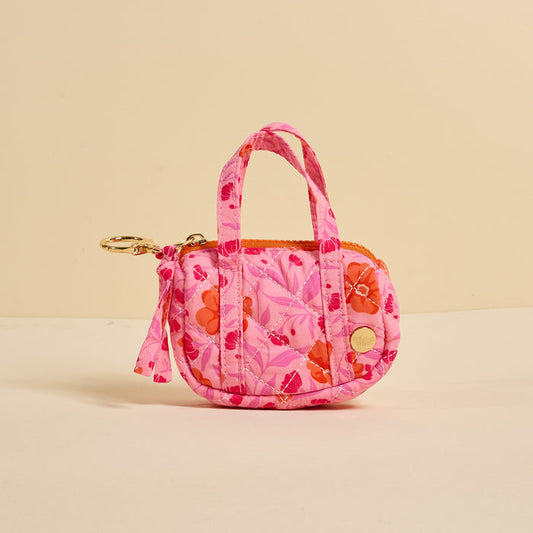 The Darling Effect’s Poppin' Petals Hot Pink Itty Bitty Duffle Bag Charm is a small quilted floral coin purse with two handles, zipper closure, and gold keychain clip—stylishly shown on a plain beige background.