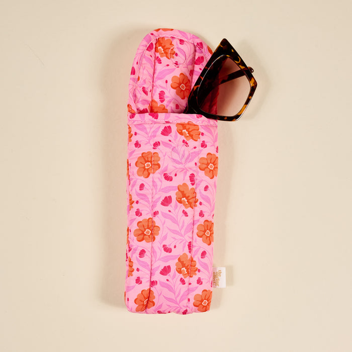 The Darling Effect’s Poppin' Petals Hot Pink Puffy Sunglasses Case features a bold orange and pink floral print, quilted design, and magnetic flap closure. Shown here with tortoiseshell sunglasses inside.