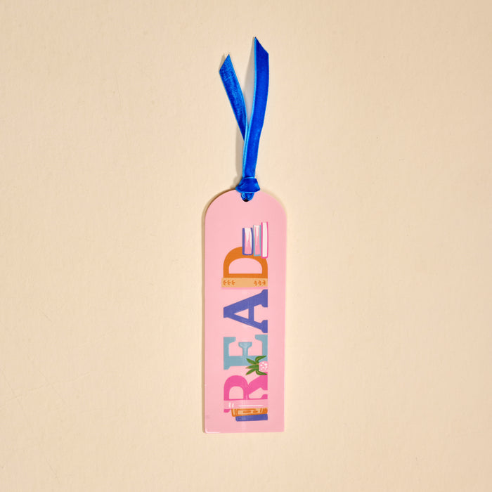 The Darling Effect’s Read Acrylic Bookmark features pink acrylic, colorful "READ" lettering, book images, and a blue velvet ribbon tassel—making it the perfect gift for book lovers.