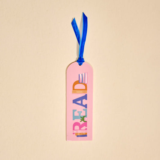The Darling Effect’s Read Acrylic Bookmark features pink acrylic, colorful "READ" lettering, book images, and a blue velvet ribbon tassel—making it the perfect gift for book lovers.