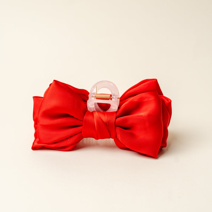 The Darling Effect Red Satin Bow Claw Clip features a bow design in satin fabric with a clear plastic clasp and gold spring.