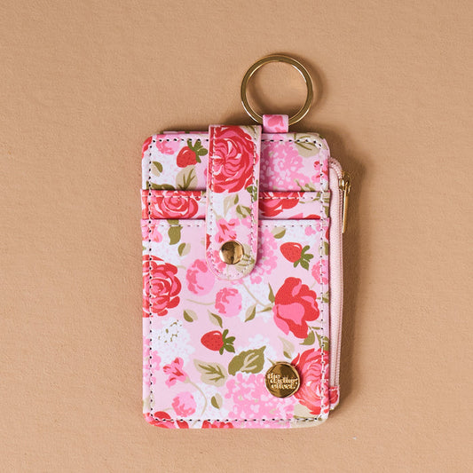 The Darling Effect's Rose Garden Keychain Wallet is a pink floral card holder with roses, strawberries, a gold keyring, and zipper closure—blending elegance and practicality for your daily essentials.
