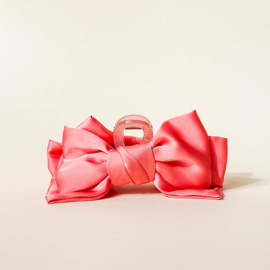 The Darling Effect's Rose Satin Bow Claw Clip is a large translucent pink hair claw topped with a satin bow, ideal for updos and styled against a simple light background.