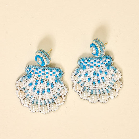 The Darling Effect’s Seashell Beaded Earrings feature white, blue, and turquoise patterns with round pearl-like beads along the bottom edge, shown on a light beige background.