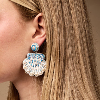 Close-up of a blonde-haired person wearing The Darling Effect’s Seashell Beaded Earrings, featuring large hand-beaded seashells with blue, white, and pearl accents.