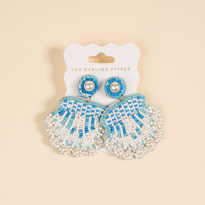 Seashell Beaded Earrings by The Darling Effect feature playful blue and white beaded shells with pearl accents, displayed on a white card labeled with the brand name.