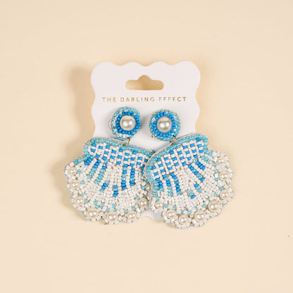 Seashell Beaded Earrings by The Darling Effect feature playful blue and white beaded shells with pearl accents, displayed on a white card labeled with the brand name.