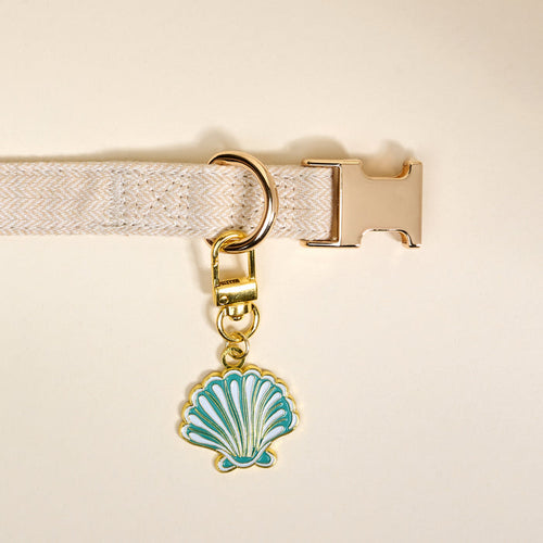 The Darling Effect’s Seashell Pawfect Collar Charm features a blue and white enamel seashell with a gold keychain, perfect for adding coastal flair to your pet’s collar or pairing with other charms.