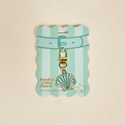 A pastel green, scalloped card from The Darling Effect displays the Seashell Pawfect Collar Charm—a teal and white seashell with a gold clasp. The card features a cat and dog illustration, making it a cute pet accessory addition.