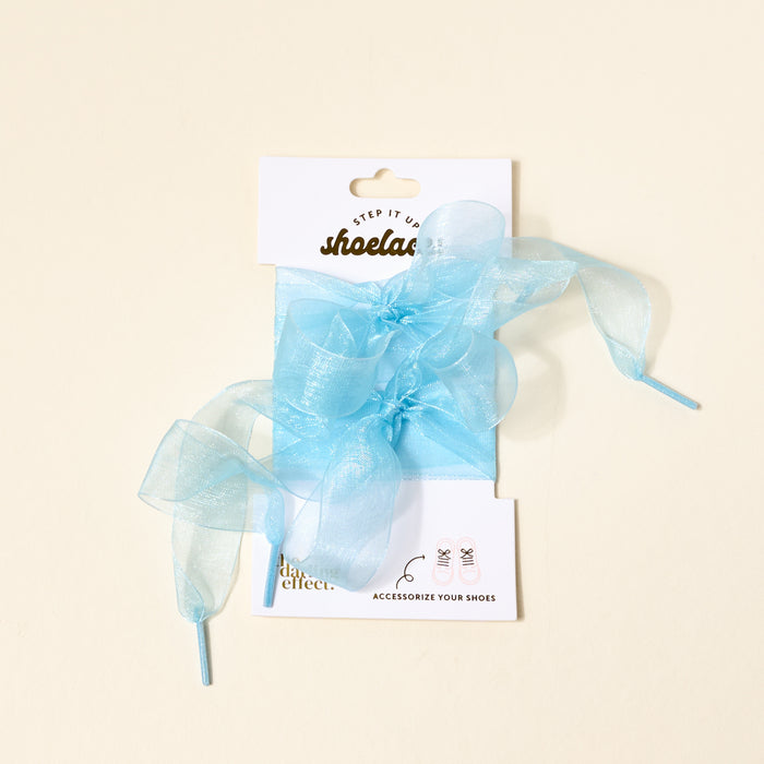 A pair of Sheer Blue Step It Up Shoelaces by The Darling Effect, tied in bows on a white card labeled "shoelaces" and "ACCESSORIZE YOUR SHOES," are displayed against a cream background.