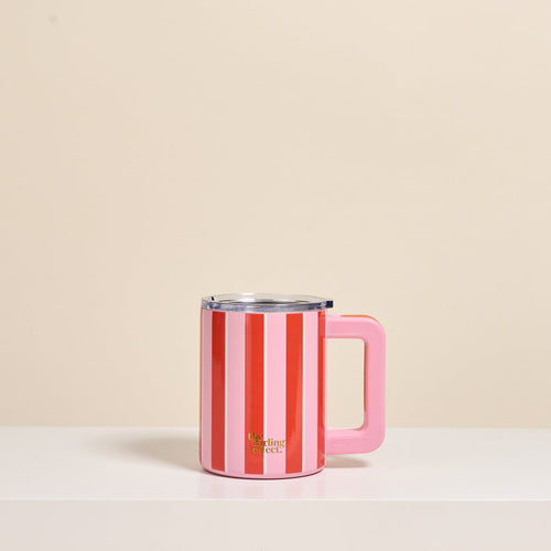 The Darling Effect Sicily Stripes Pink 14 oz Insulated Mug, featuring vertical pink and red stripes, a solid pink handle, clear lid, double-wall insulation, and gold branding near the base, sits on a white surface against a beige background.