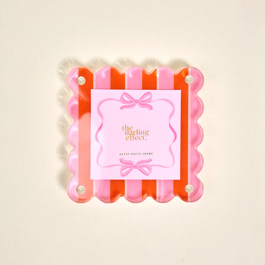 The Sicily Stripes Pink Little Moments Acrylic Picture Frame by The Darling Effect features a square scalloped-edge in pink and orange, four silver screws, a bow card insert, and a secure magnetic closure.