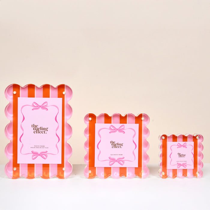 The Sicily Stripes Pink Little Moments Acrylic Picture Frames by The Darling Effect feature scalloped edges, magnetic closures, and pink papers with a bow design, available in small, medium, and large sizes against a pale background.