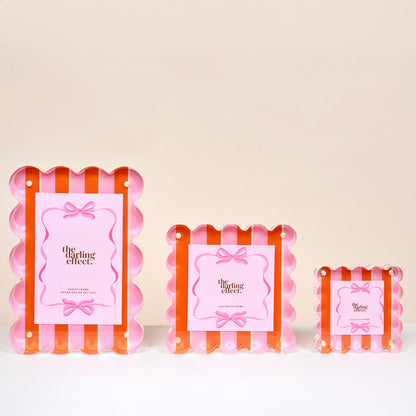 The Sicily Stripes Pink Little Moments Acrylic Picture Frames by The Darling Effect feature scalloped edges, magnetic closures, and pink papers with a bow design, available in small, medium, and large sizes against a pale background.
