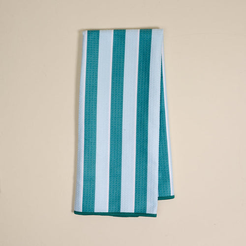 The Darling Effect Sicily Stripes Teal Waffle Tea Towel, featuring wide teal and light blue vertical stripes, is folded and displayed on a plain beige surface.