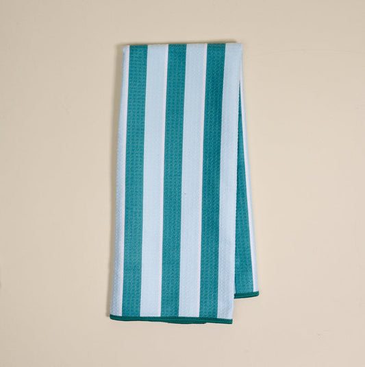 The Darling Effect Sicily Stripes Teal Waffle Tea Towel, featuring wide teal and light blue vertical stripes, is folded and displayed on a plain beige surface.