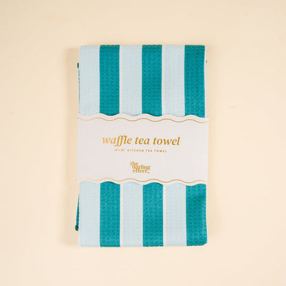 The Sicily Stripes Teal Waffle Tea Towel by The Darling Effect measures 18x25" and features teal and light blue stripes—an absorbent, stylish addition to any kitchen.