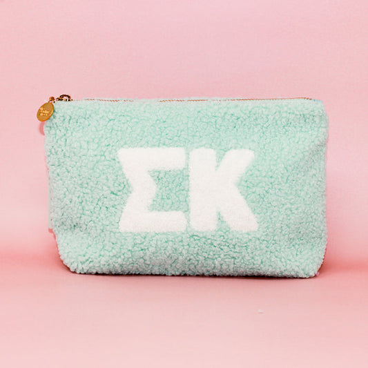The Darling Effect Sigma Kappa Aqua Teddy Letter Pouch features crisp white Greek letters on mint green fuzz, photographed on pastel pink—a cute accessory for sorority sisters or teddy pouch fans.