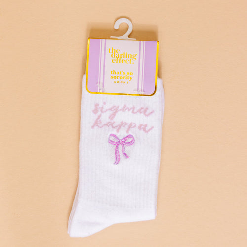 Sigma Kappa Embroidered Crew Socks by The Darling Effect: white socks feature pink Sigma Kappa embroidery, a bow, and come with a lavender and gold tag labeled "that's so sorority spirit SOCKS.