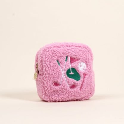 The Darling Effect’s Square The Golf Edit Teddy Pouch is a small pink sherpa pouch featuring embroidered golf clubs, a green patch, pink flag, white ball, and a round gold zipper pull—perfect for on-the-go organization.