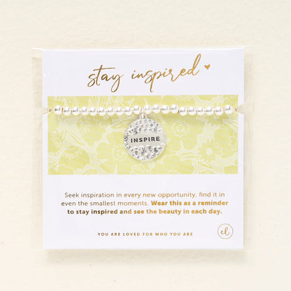 The Darling Effect's Stay Inspired Beaded Charm Bracelet features a hammered INSPIRE charm and comes on a card reading "stay inspired"—a meaningful gift to remind you to seek inspiration and appreciate the beauty each day brings.