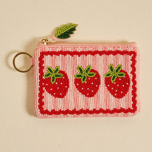 The Darling Effect’s Strawberries Handcrafted Beaded Pouch is a pink coin purse with a gold keyring, beaded strawberries, green leaf zipper charm, and red scalloped border.