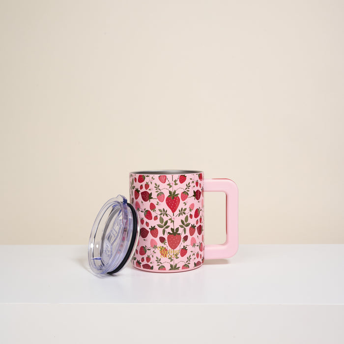 The Darling Effect’s Strawberry Fields 14 oz Insulated Mug has double-wall insulation, a rectangular handle, a white surface with red, pink, and yellow floral patterns, and comes with a transparent lid resting beside it.