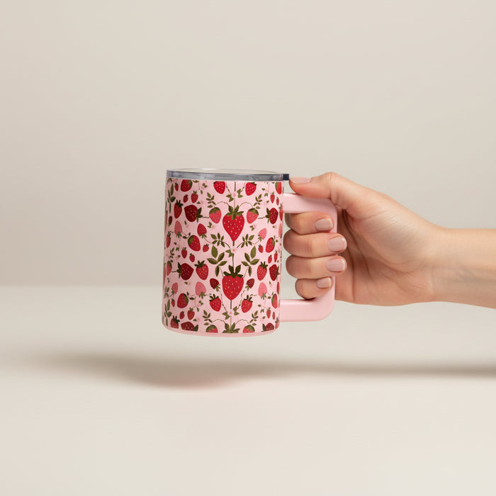 A hand holds The Darling Effect’s Strawberry Fields 14 oz Insulated Mug, decorated with strawberries, flowers, and green leaves, against a plain light background.