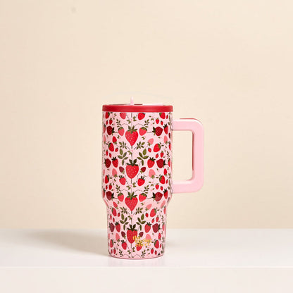 The Darling Effect's Strawberry Fields 20 oz Lifestyle Flip Straw Tumbler—a pink insulated stainless steel tumbler with a handle, decorated with strawberries and small flowers—sits on a white surface against a beige background.