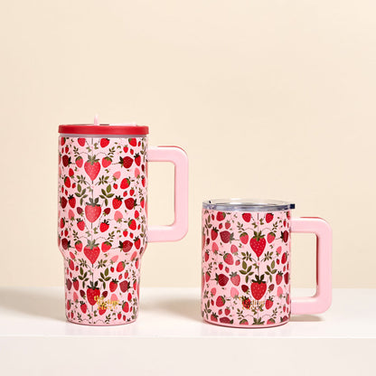 Two pink mugs with handles from The Darling Effect—one a tall Strawberry Fields 20 oz Lifestyle Flip Straw Tumbler (insulated stainless steel with lid), the other shorter and lidless—display strawberries and hearts on a white surface against a beige background.